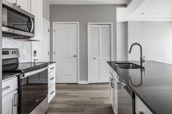 A kitchen with black counter tops and white cabinets and a sink
